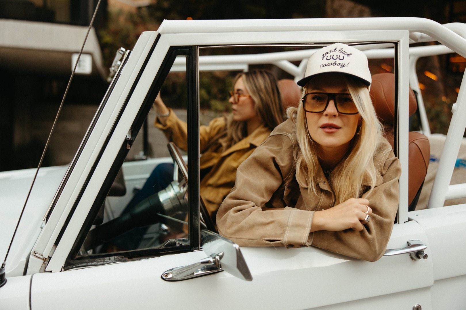 A woman with a hat and sunglasses looks out through the open window of a rugged jeep.